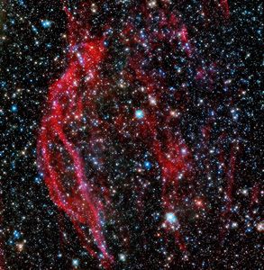 A field full of stars of all different colors, with several deep red tendrils/streaks of gas running from top to bottom near the center.